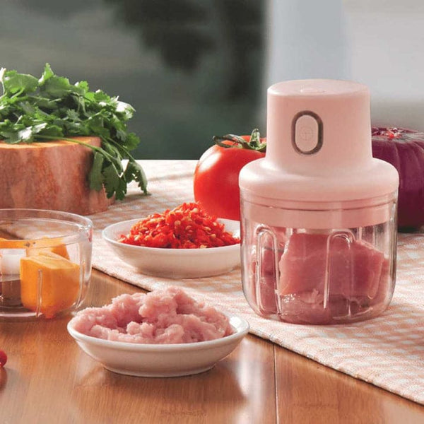 compact mini food chopper placed on a kitchen table with chopped ingredients and vegetables around it.